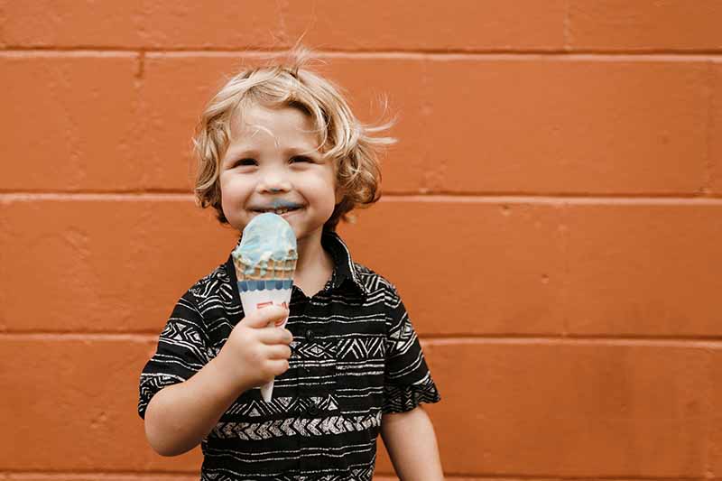 Ppicture of a small child eating icecream against an orange wall