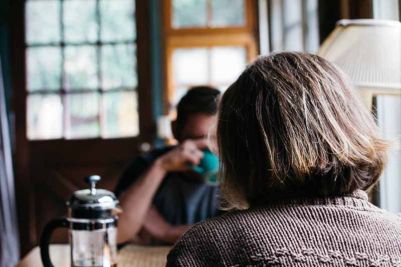 Picture of a lady in brown jumper siting at the breakfast table with her husband