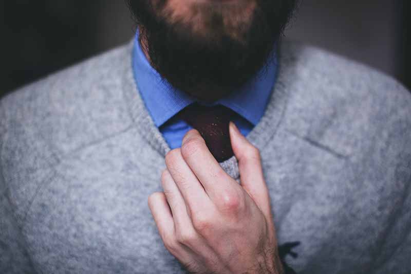 Picture of man with a beard adjutsing his tie