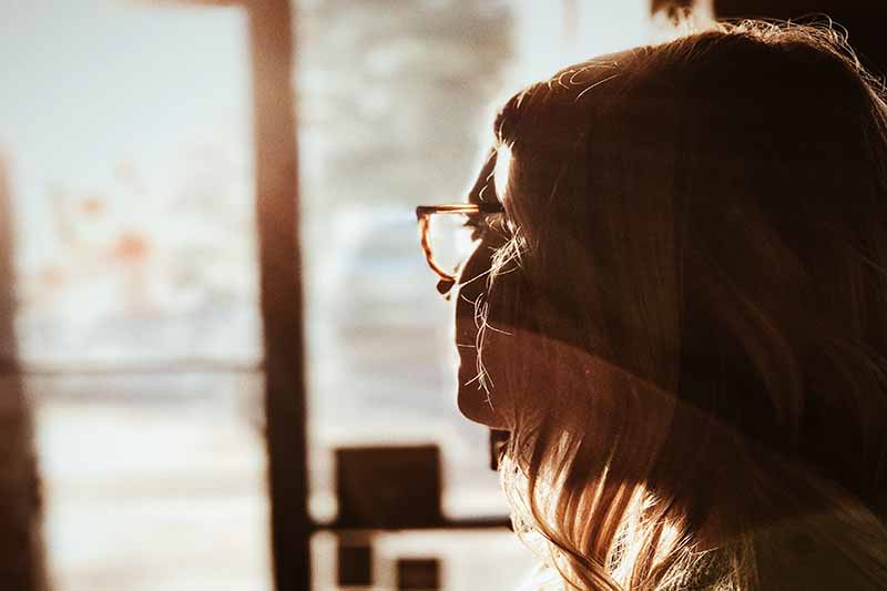 Picture of a woman with glasses gazing out a window with sunlight