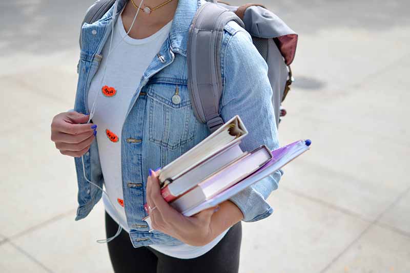 Picture of a girl in a denim jacket carrying text books