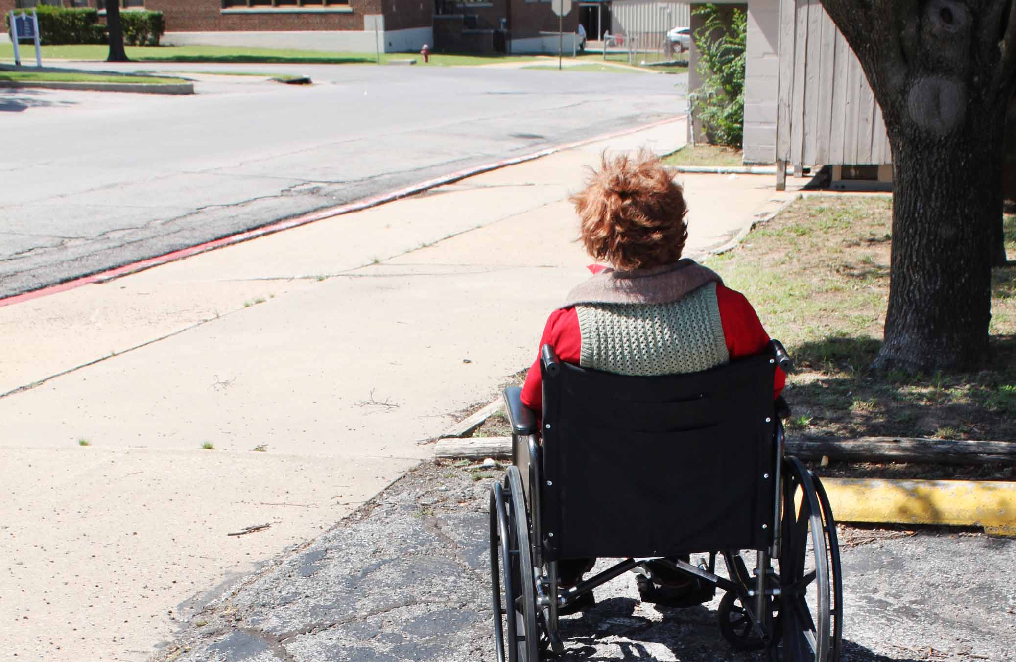 Picture of a woman wearing a red top sitting in a wheelchair at the front of a resifential care facility