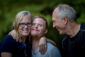 Picture of mother and father with thier son who lives with a disabilty, laughing in the park